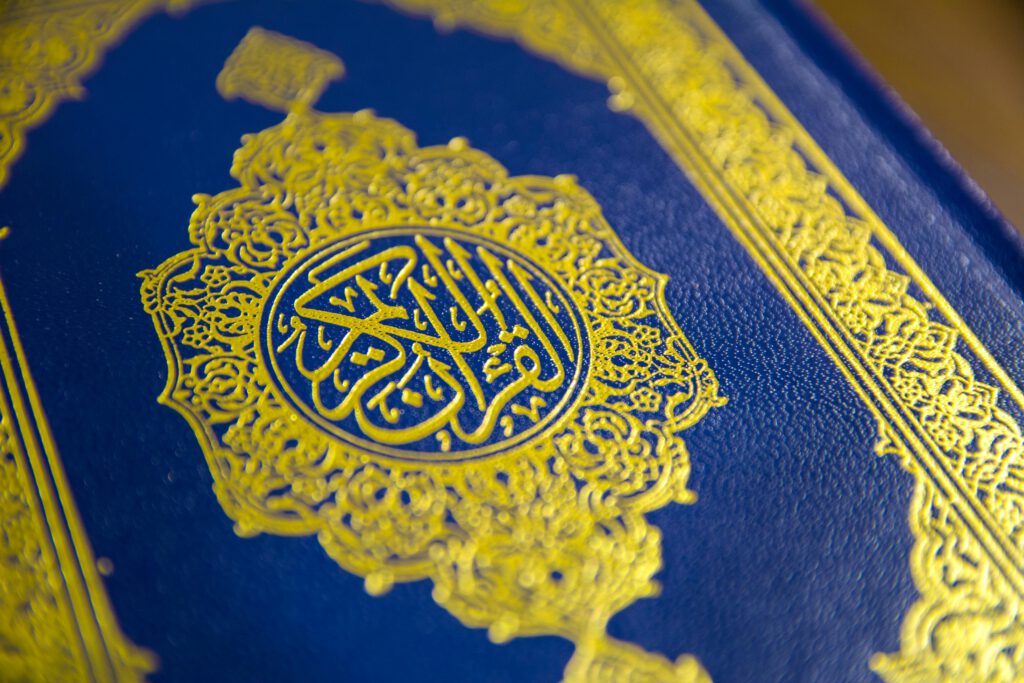 Close-up of intricate gold Quranic calligraphy on a blue cover, showcasing elegant Islamic design.